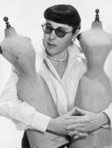 A black and white portrait of Edith Head holding two dressmakers dummies