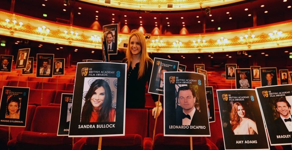 A young blonde woman places signs with showing BAFTA nominees in the red seats at the Royal Opera House