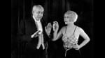 This 1920's black and white image shows a middle aged man in tails looks apprehensively at a smiling young woman.