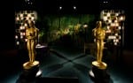 Two giant Oscars statuettes stand in a dimly lit room in front of tables, chairs and decorations.