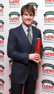 Tom Cruise holding his Empire Award in front of a white background with the Empire logo printed on it.