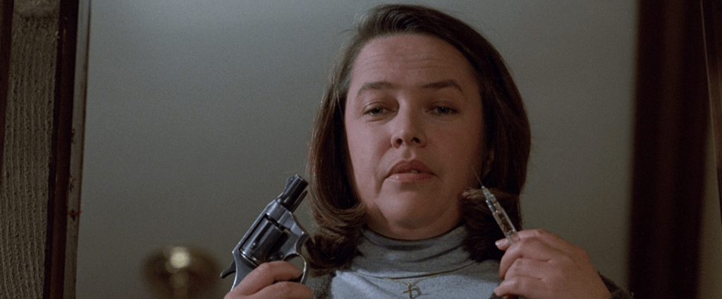Annie Wilkes holding a revolver and a syringe.